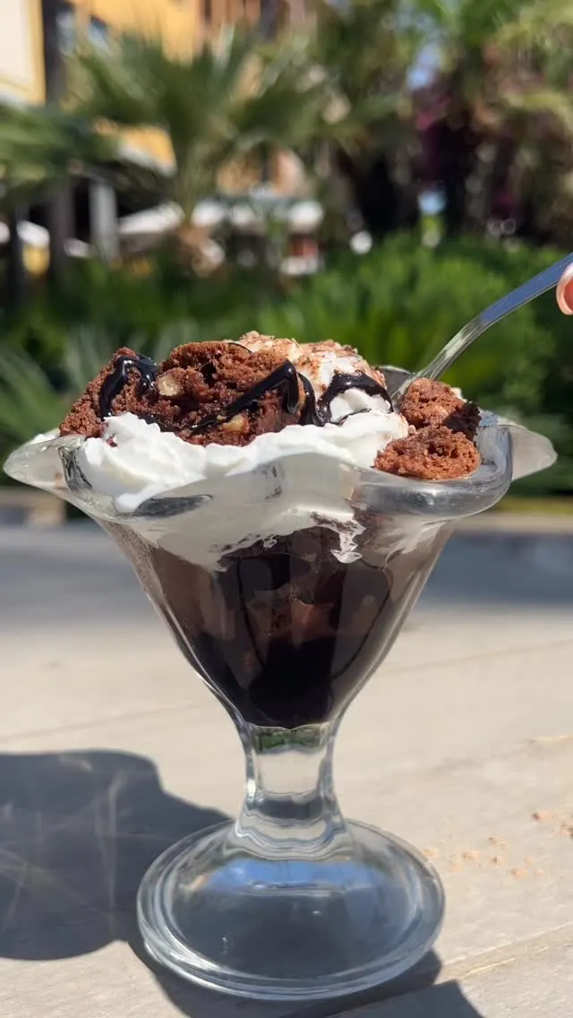 A chocolate sundae with brownie and cream on a sunlit terrace table