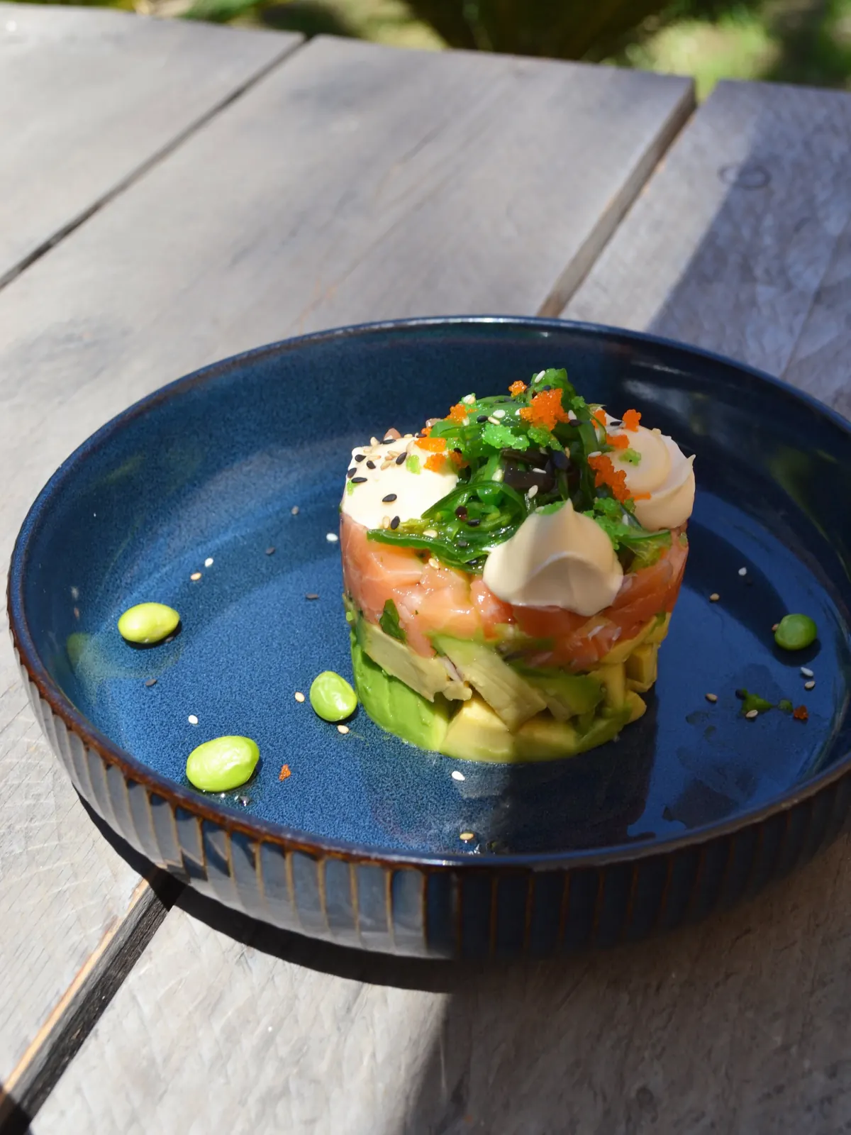 Salmon tartare on a deep blue plate with avocado and tobiko