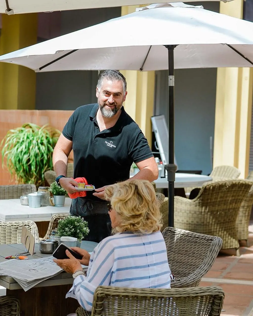 A waiter serving a guest at a table under a parasol